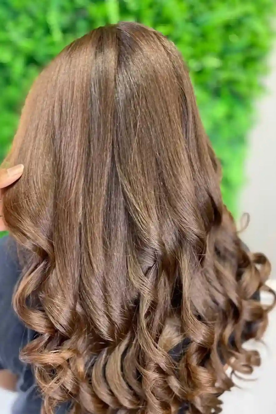 Person with long, wavy brown hair against a blurred green and white background