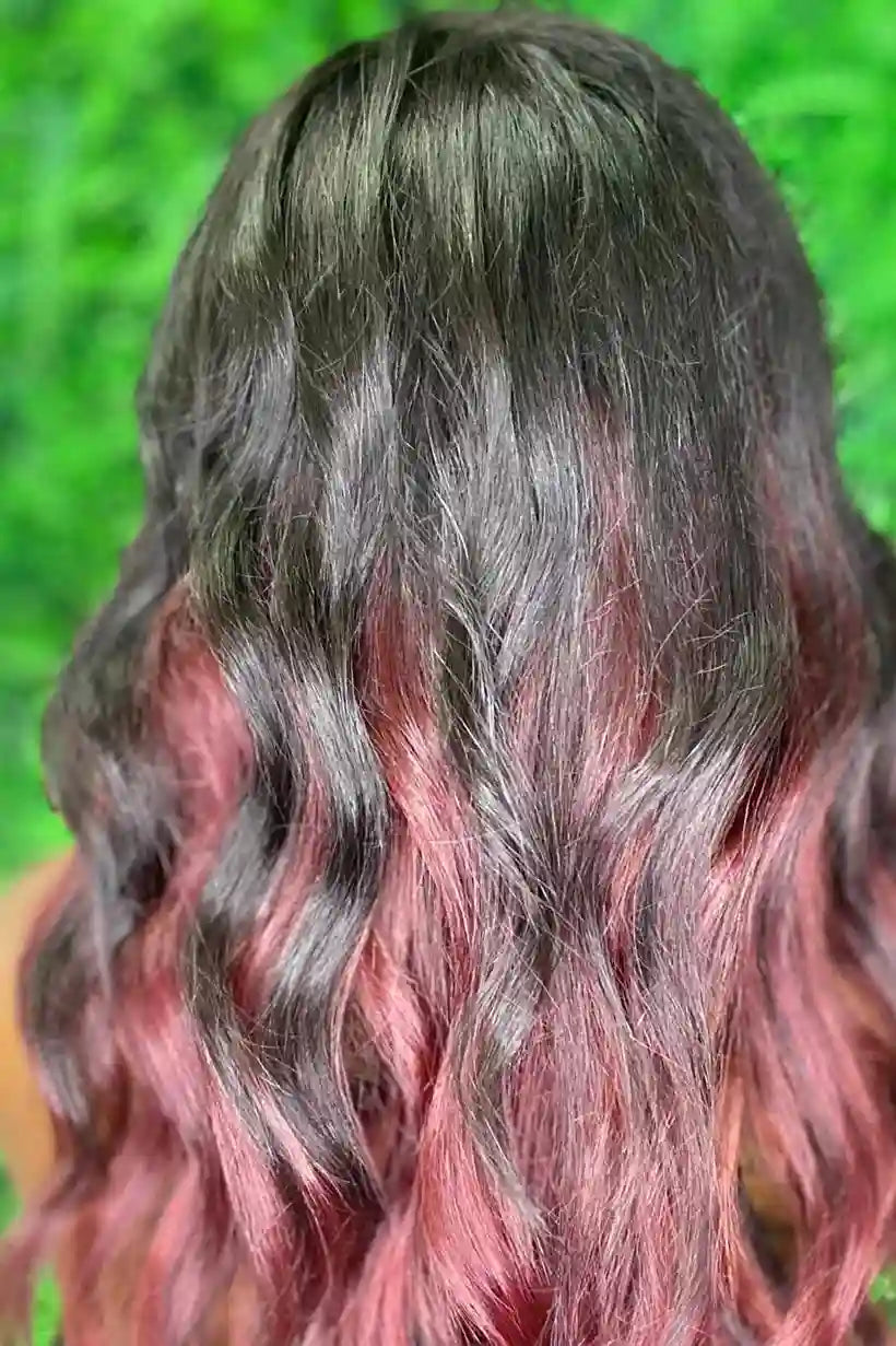 Close-up of wavy hair with black and pink coloration against a green leafy background