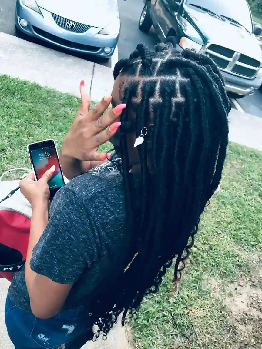 Person with braided hair holding a phone outdoors