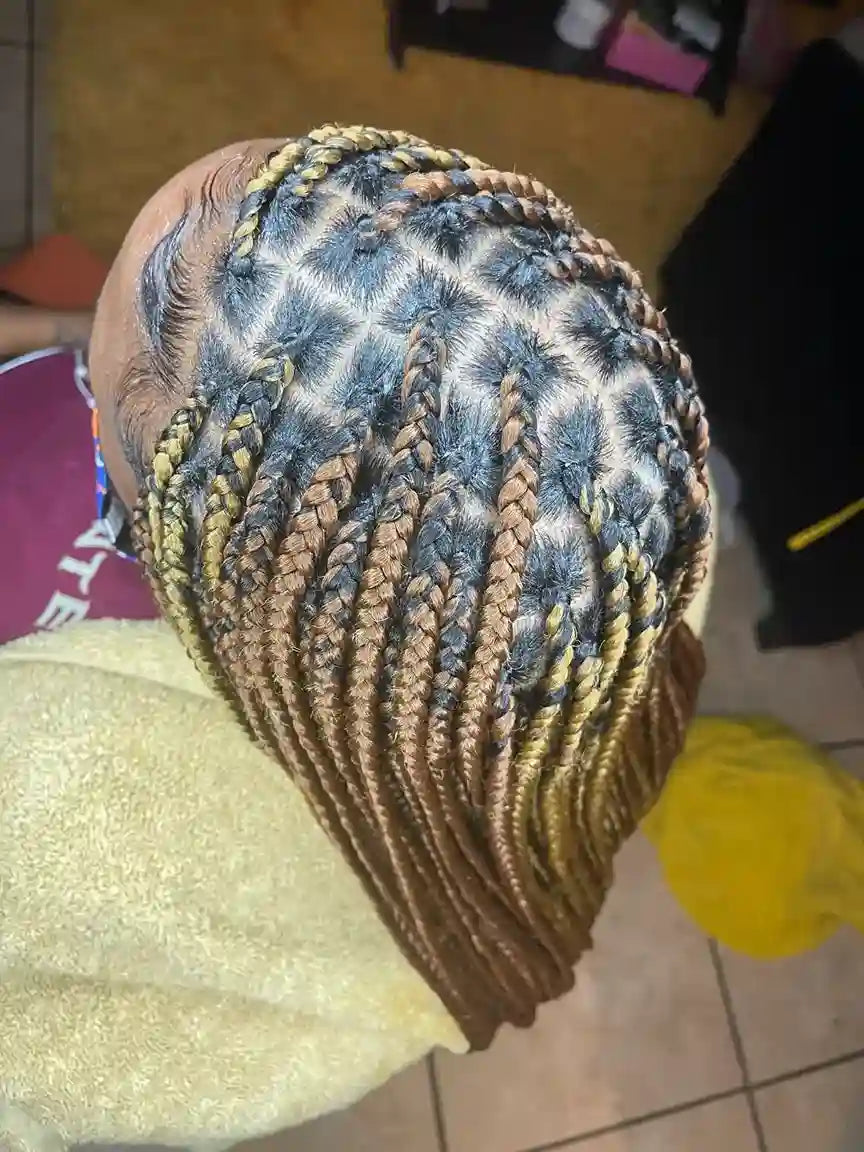 Close-up of a person with braided hair, wearing a brown headscarf, on a tiled floor.