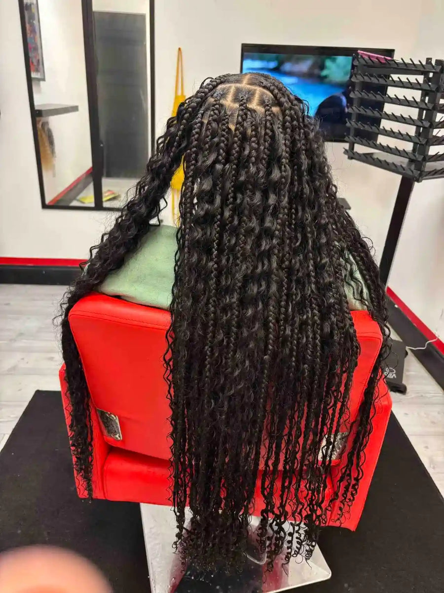 Person with long braided hair sitting in a red chair in a salon setting.
