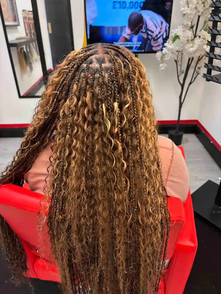 Person with long, curly hair sitting in a salon chair with a TV screen in the background.