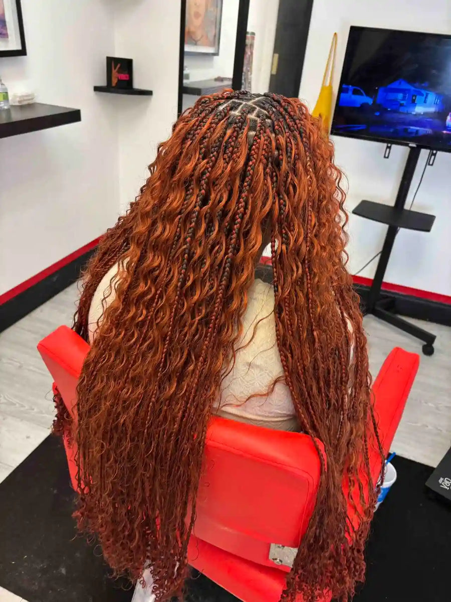 Person with long, braided hair sitting in a salon chair with a TV in the background.