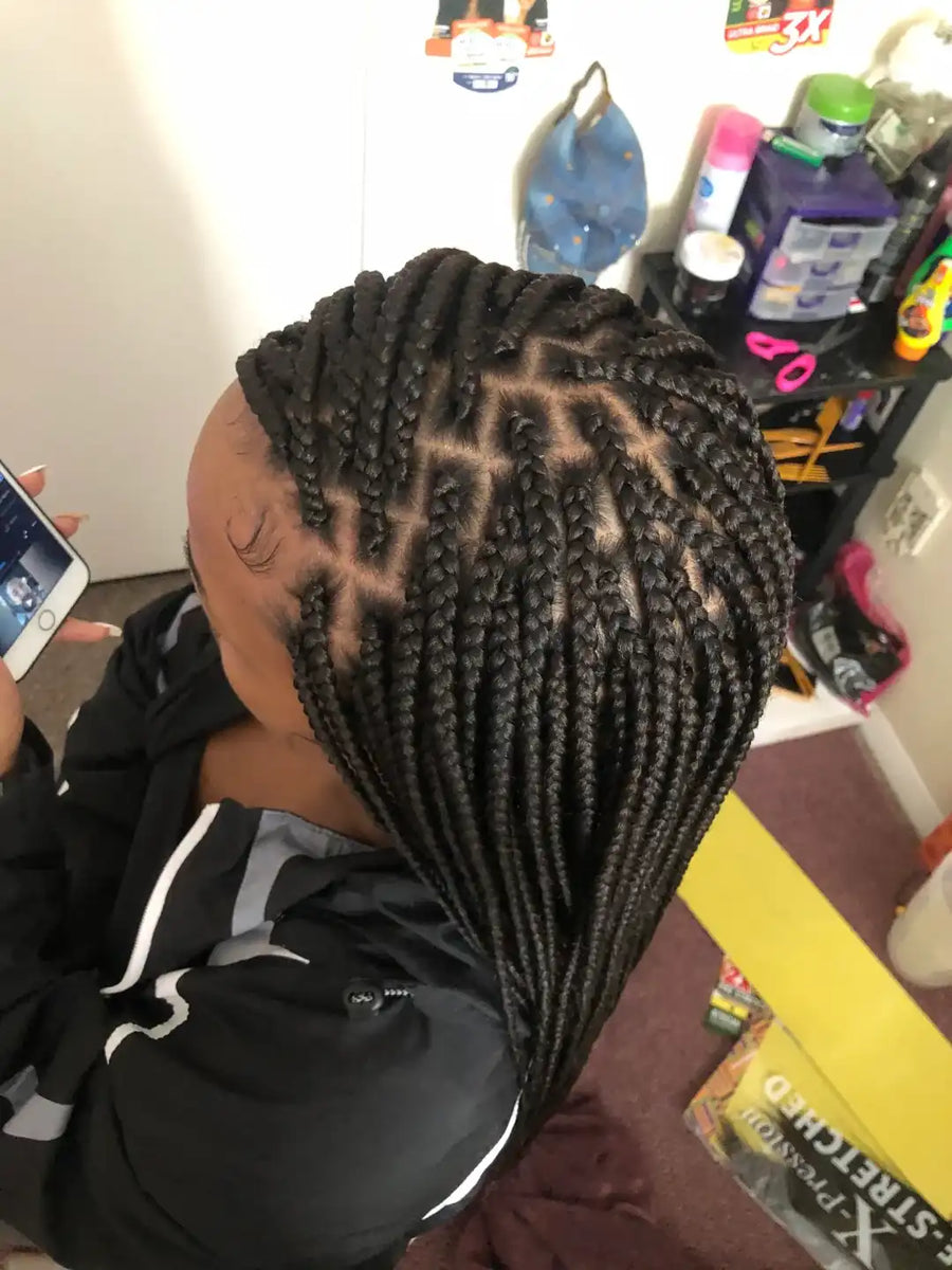 Person with braided hair taking a selfie in a salon setting.