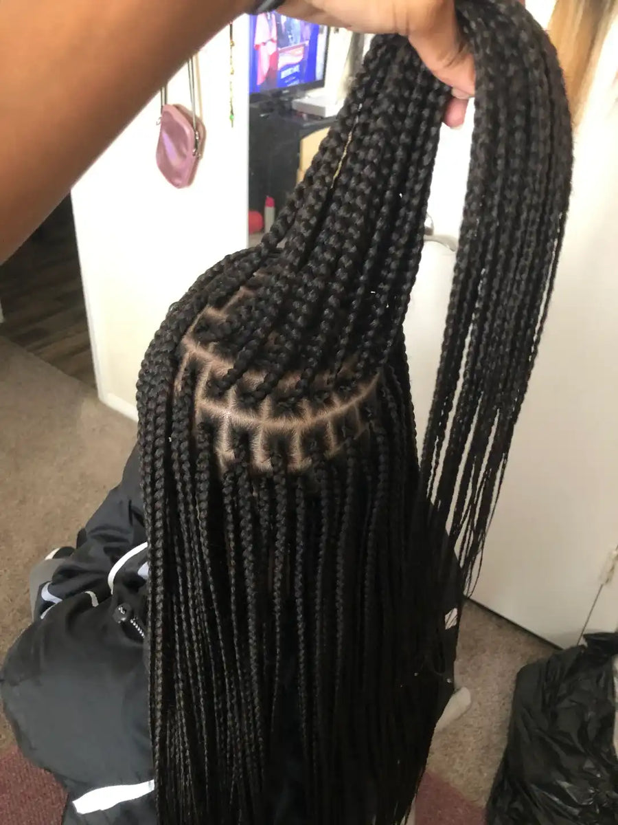 Black braided hair extensions held by a person indoors.