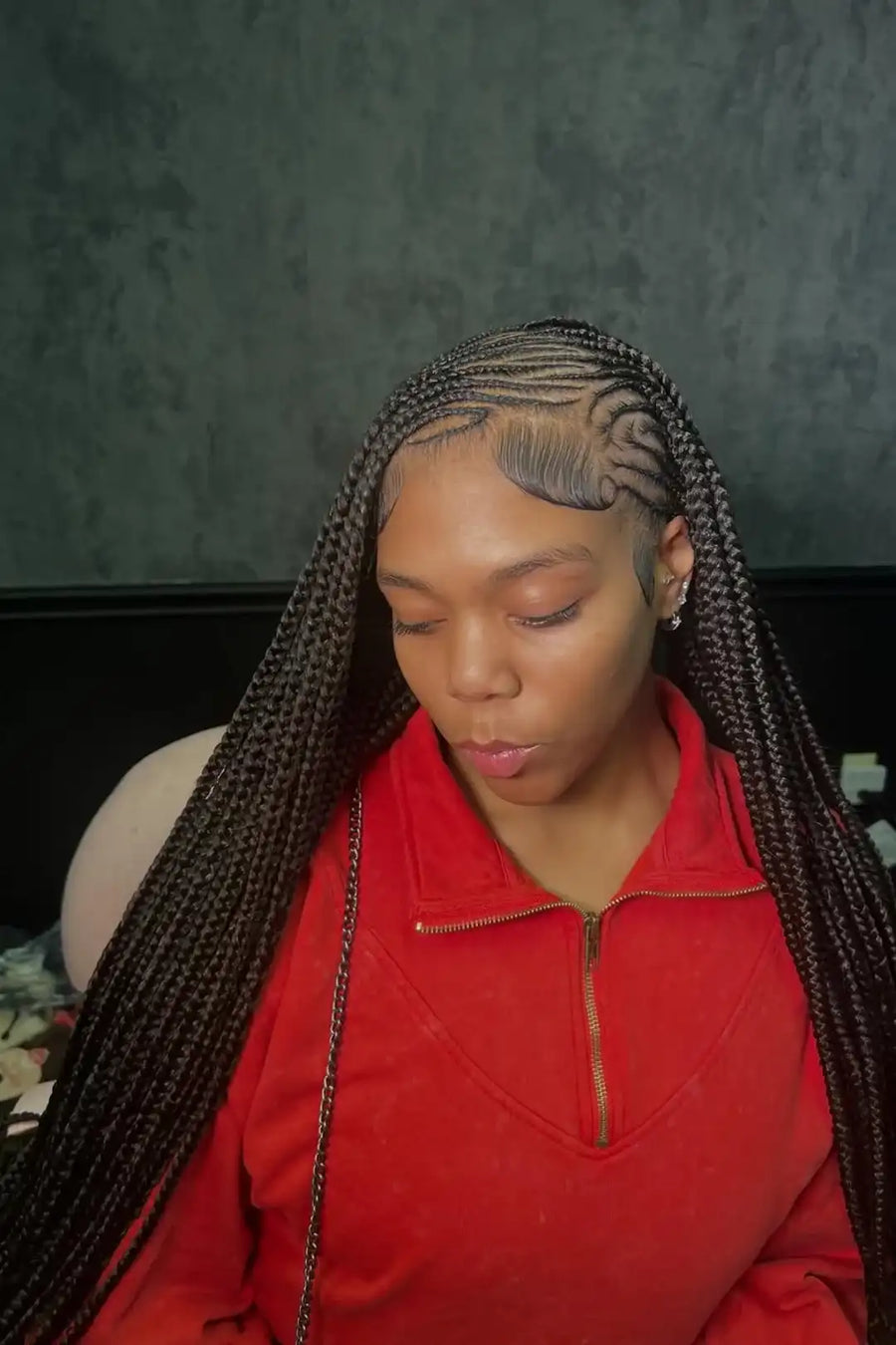 Person with braided hair wearing a red shirt against a dark background