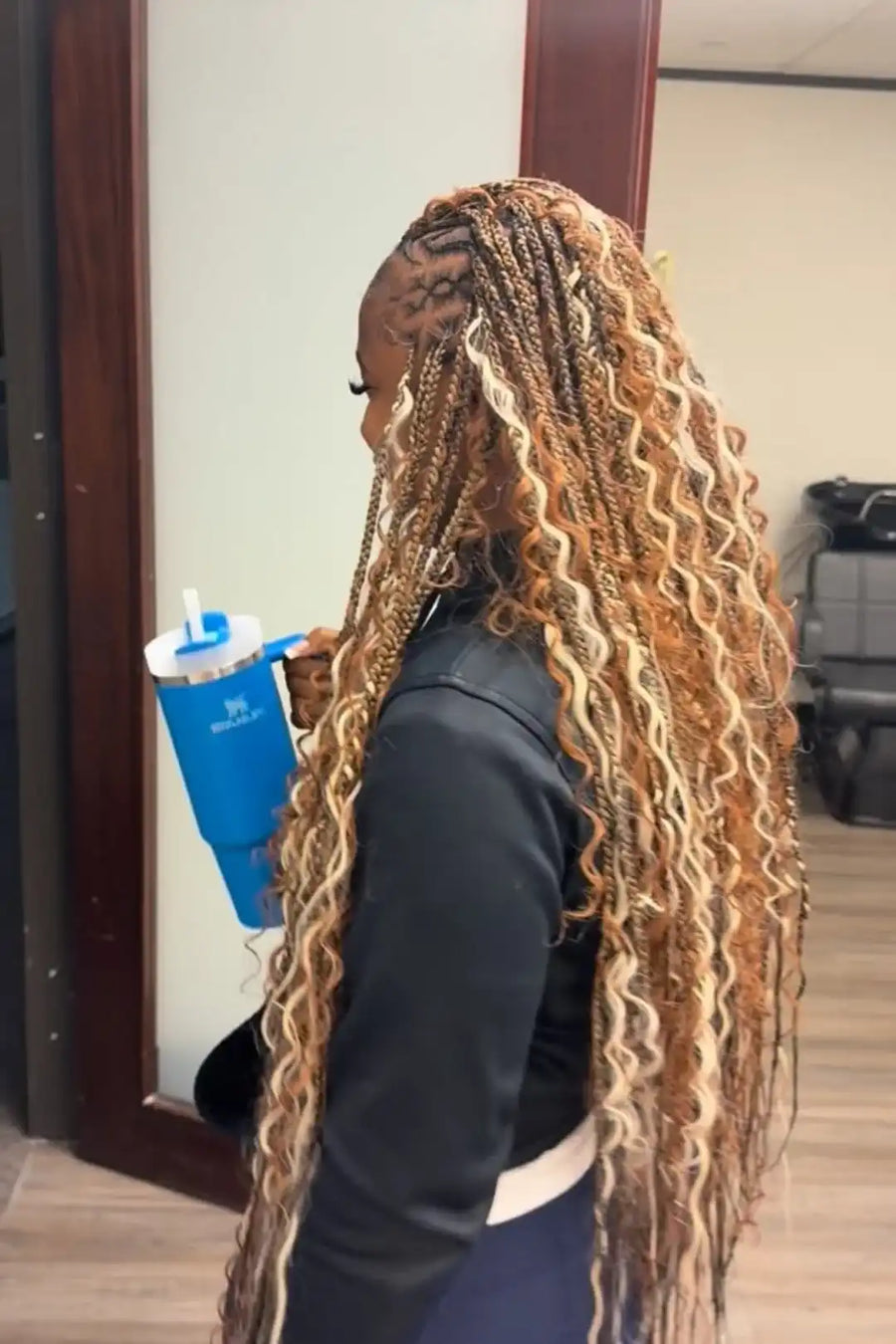 Person with long braided hair holding a blue water bottle in an indoor setting.