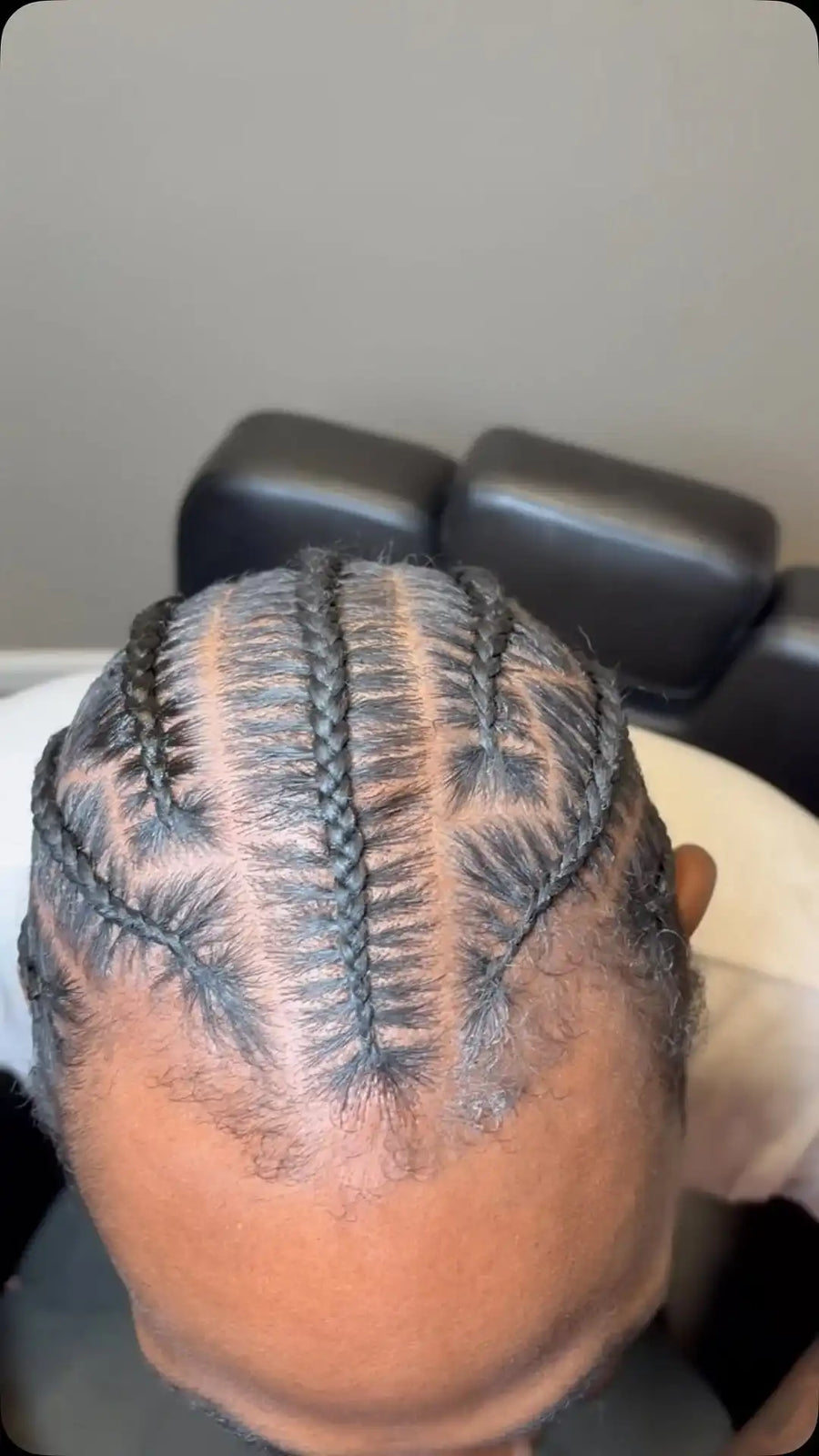 Top-down view of a person's head with intricate braided cornrow hair extensions, showing the detailed weave pattern against a neutral indoor background.