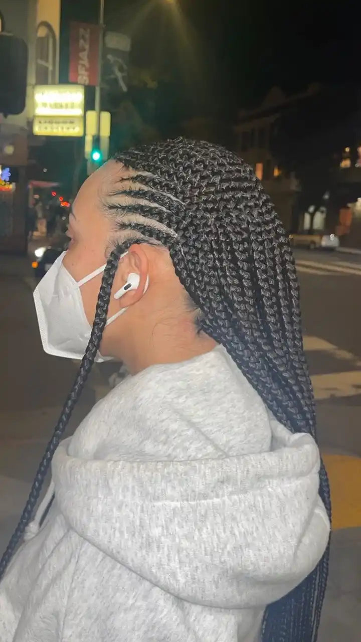 Person with braided hair wearing a face mask and earphones on a street at night.