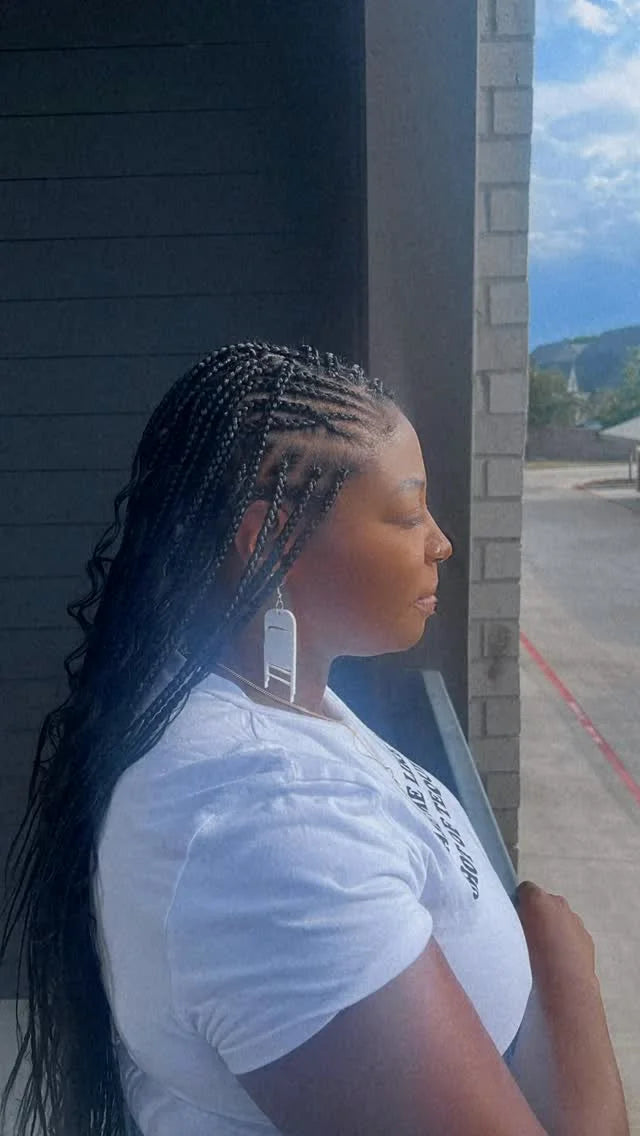 Woman with braided hair wearing a white shirt standing outside.