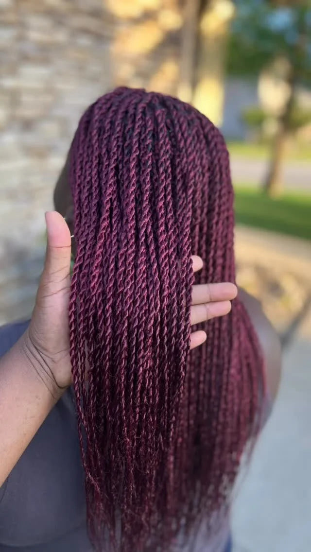 Maroon braided hair held by a person outdoors with blurred background