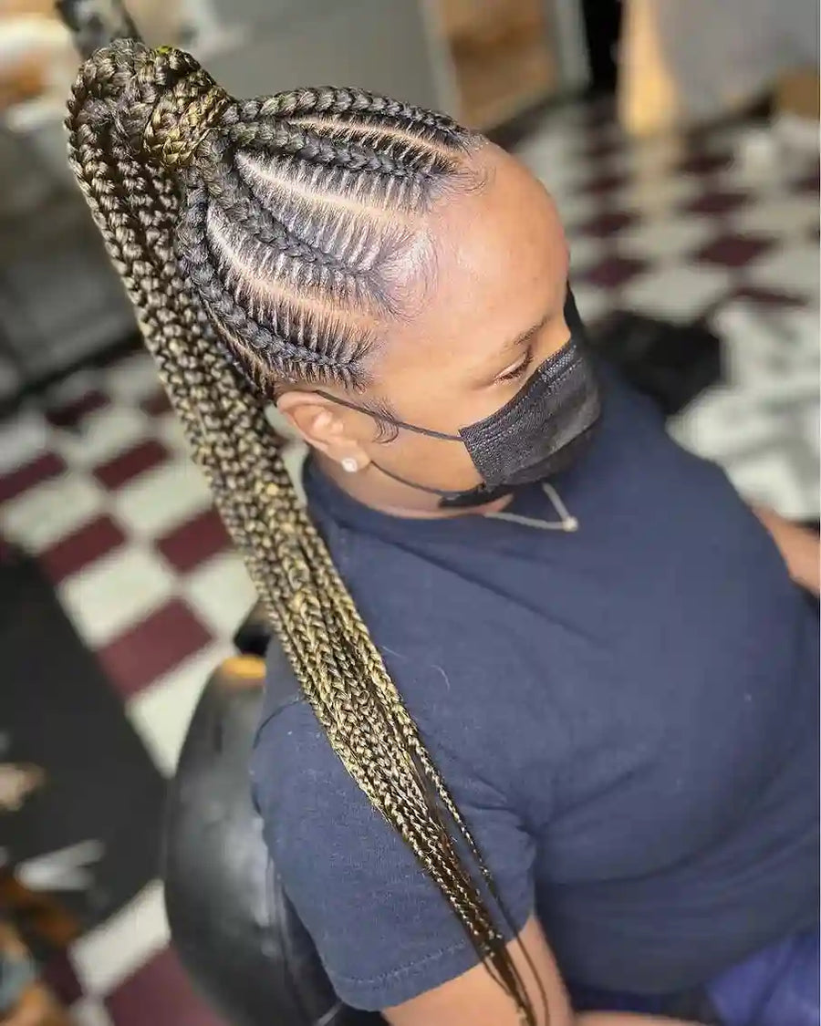 Person with braided hair sitting in a chair, wearing a face mask.