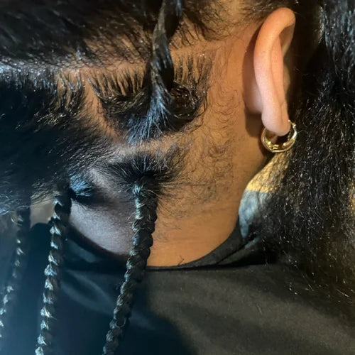 Close-up of an ear with a gold earring and braided hair.