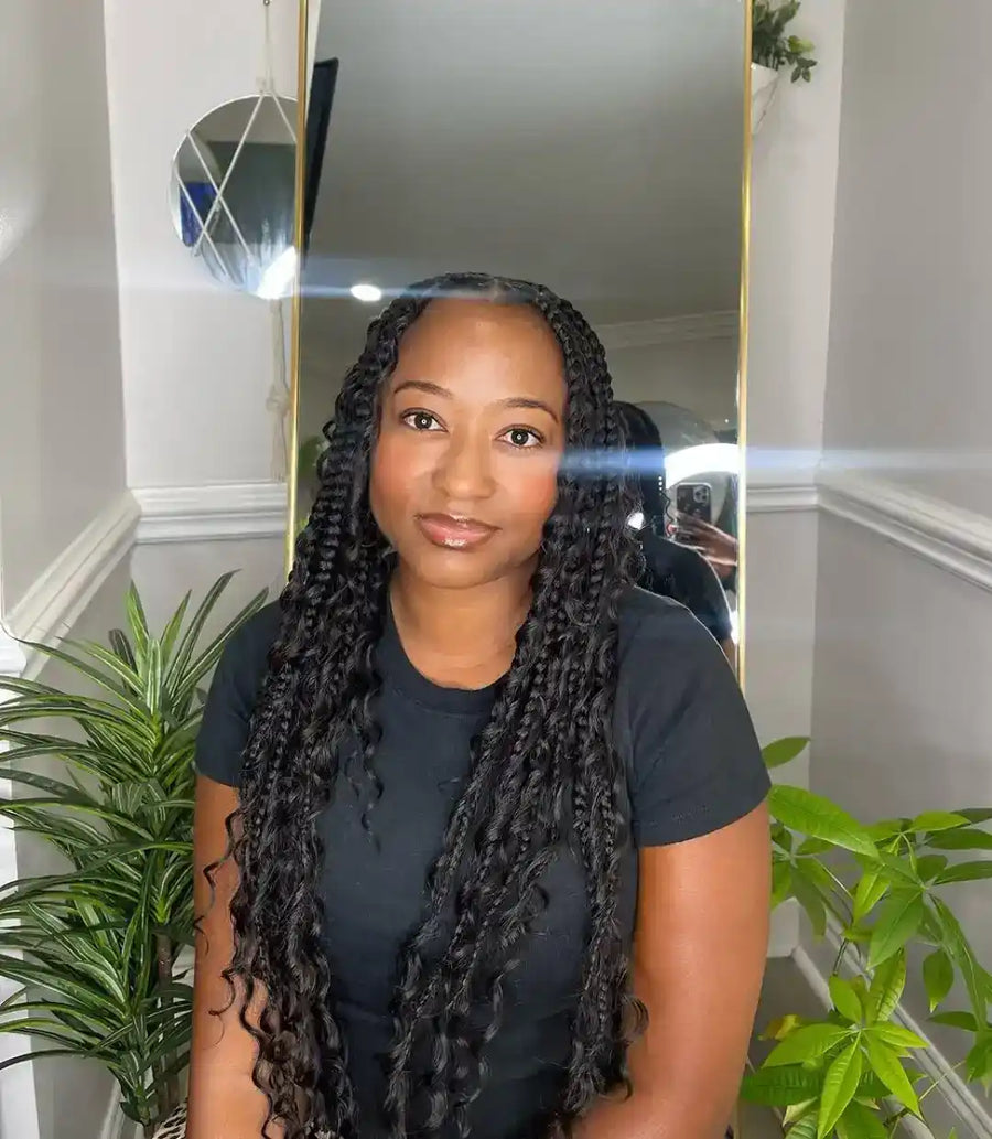 Woman with braided hair standing in front of a mirror in a room with plants.
