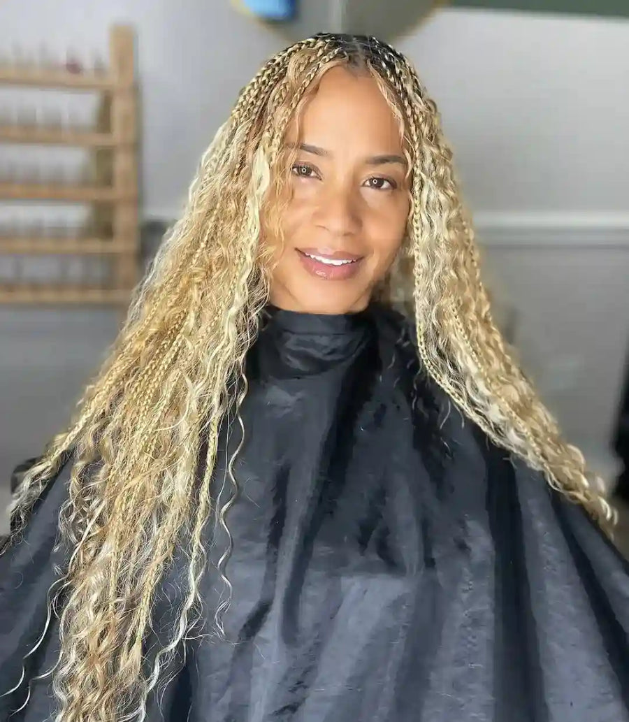 Woman with long blonde braided hair wearing a black salon cape.