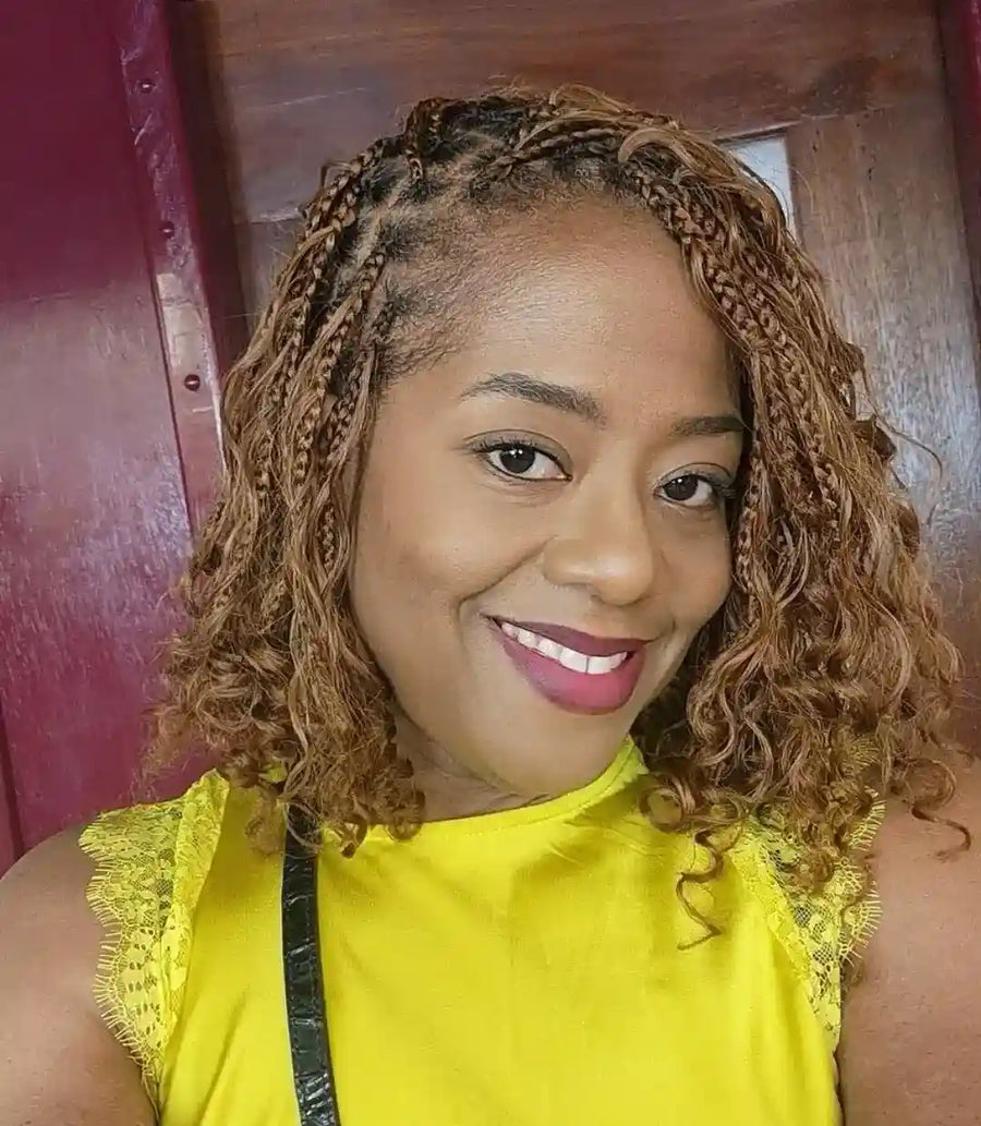 Woman with braided hair wearing a yellow top in front of a wooden door.