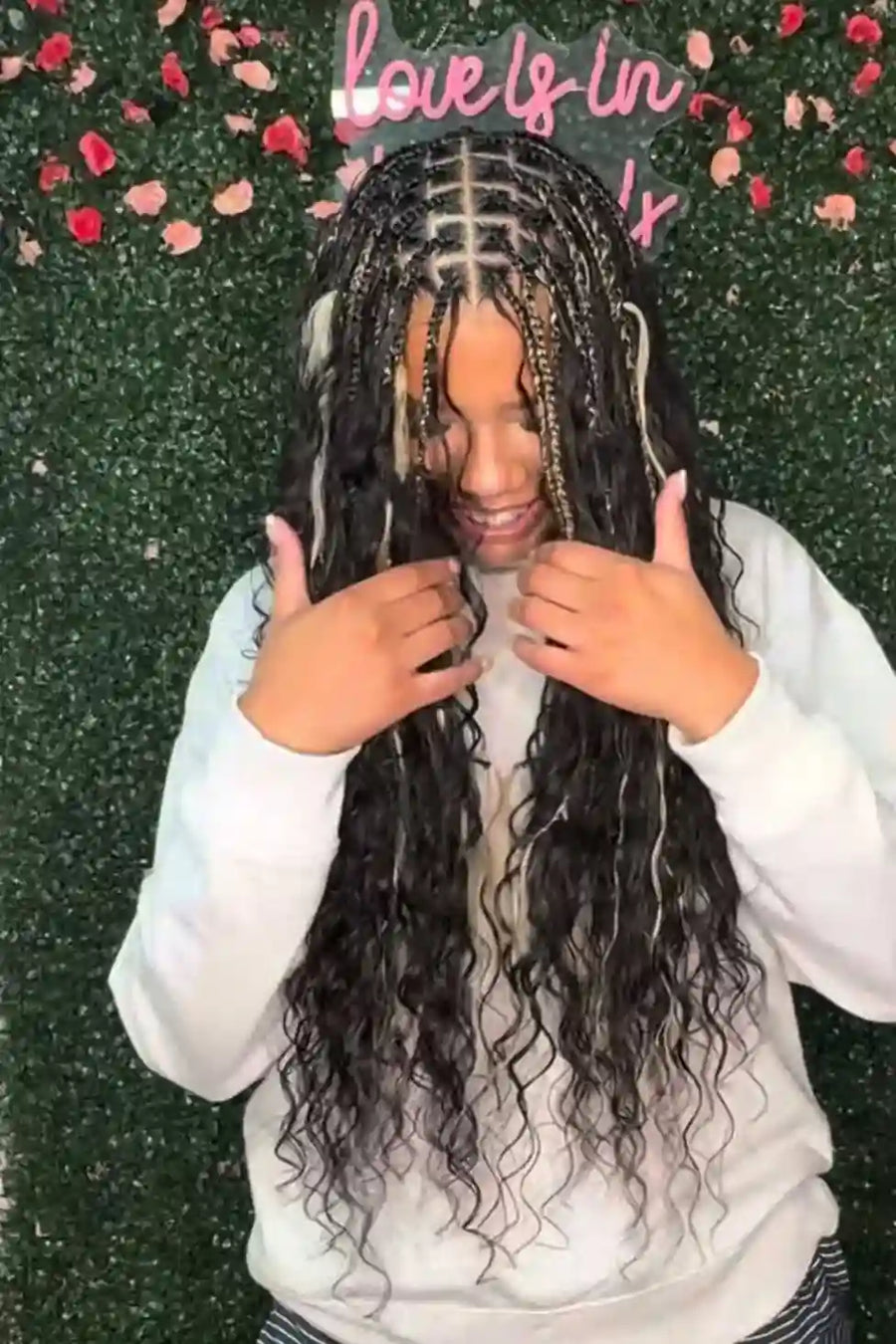 Person with styled hair giving a thumbs-up gesture against a decorative background with 'love is in the air' text.