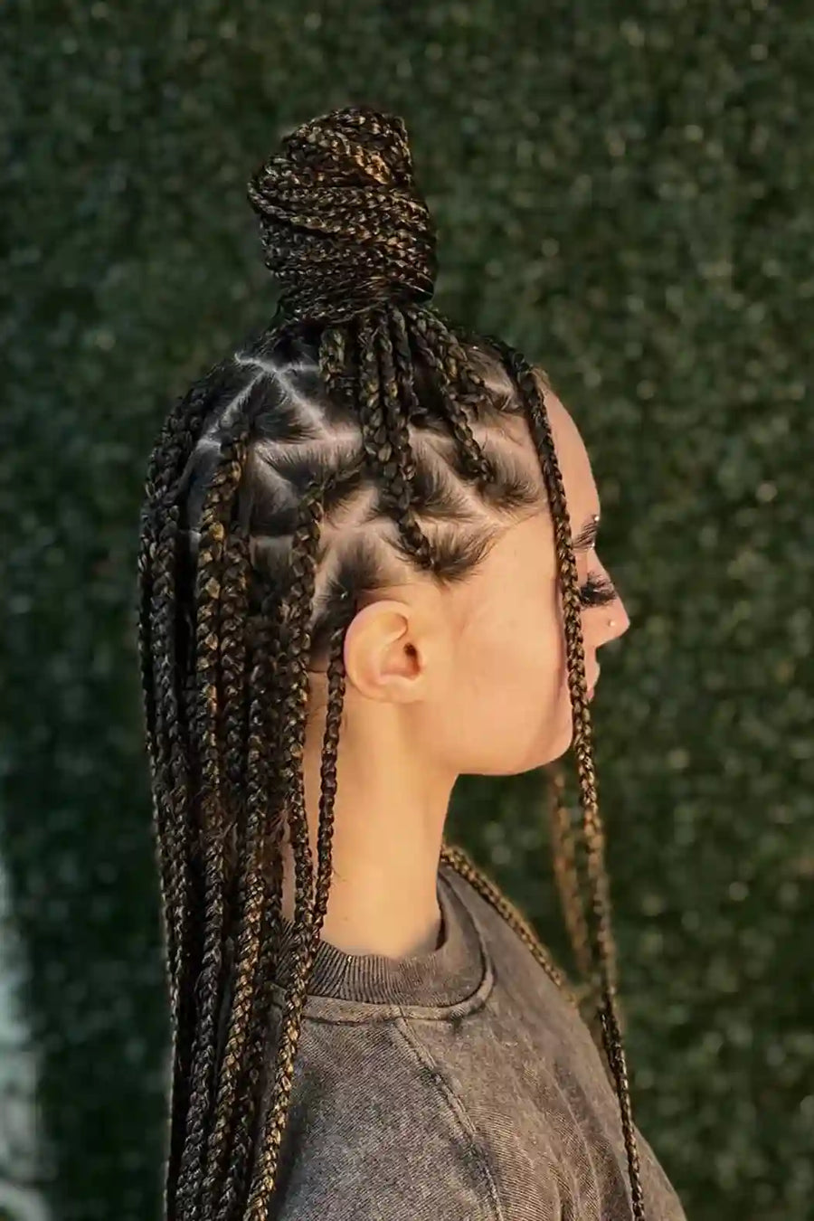 Person with braided hair styled in cornrows against a textured green wall.