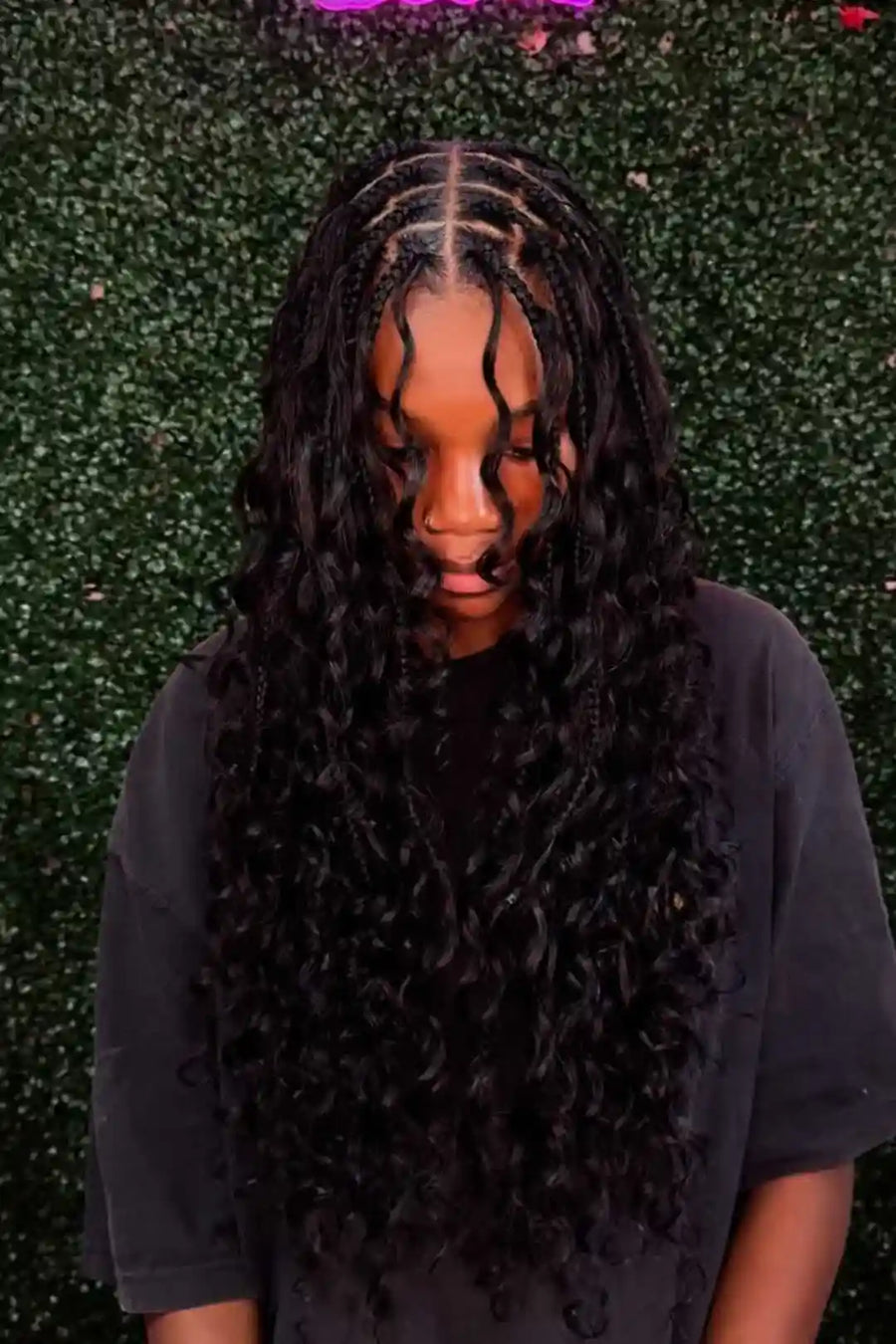 Person with braided hair covering the face against a textured green background