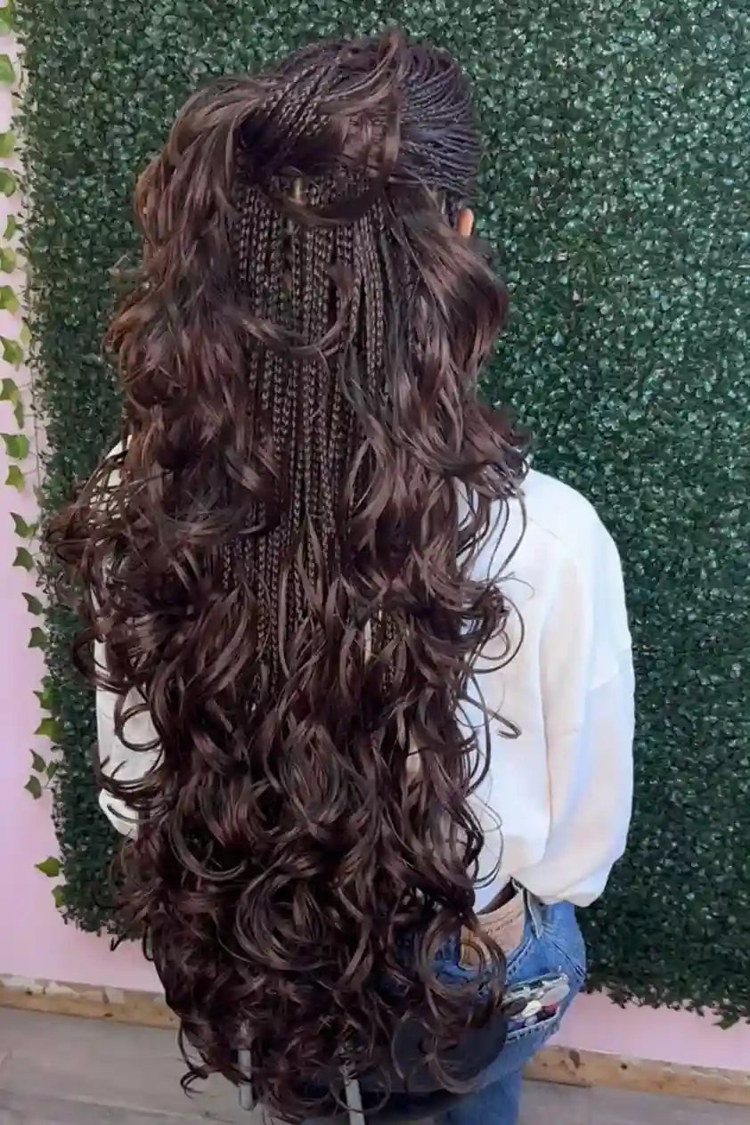Person with long, braided hair styled in loose curls against a green textured wall.