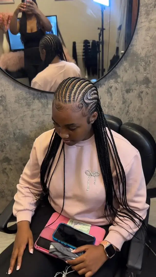 Woman with braided hair sitting in a salon chair, using a phone.