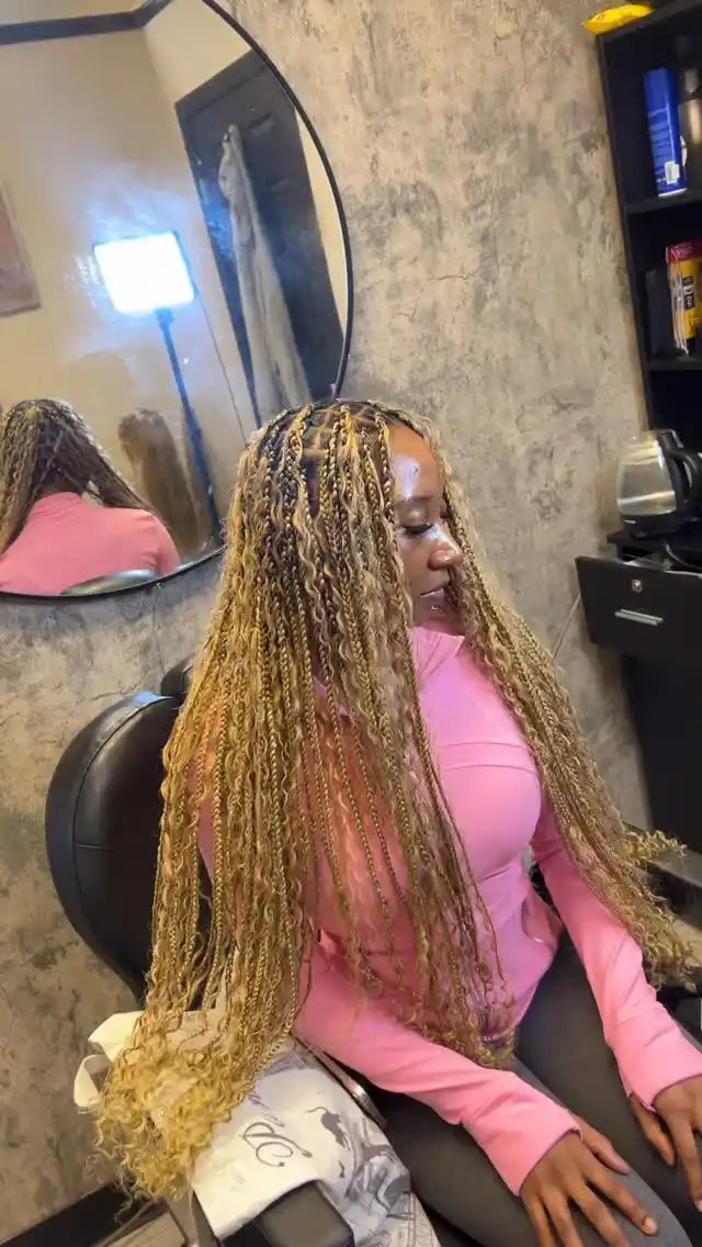 Woman with braided hair sitting in a salon chair, wearing a pink shirt.