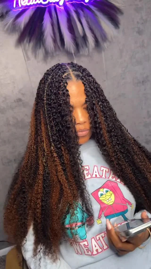 Person wearing a colorful sweatshirt with a cartoon character, holding a phone, and standing in front of a neon sign.