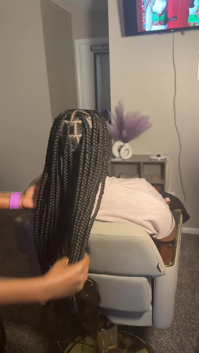 Person with braided hair in a salon setting with a TV in the background