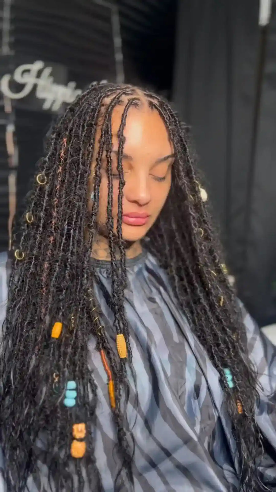 Person with styled braids wearing a salon cape against a blurred background