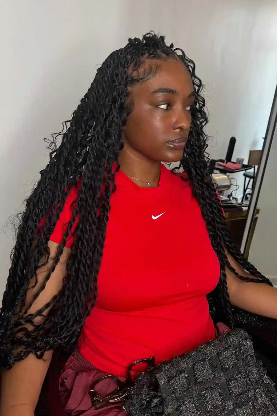Person wearing a red Nike shirt with braided hair, sitting indoors.