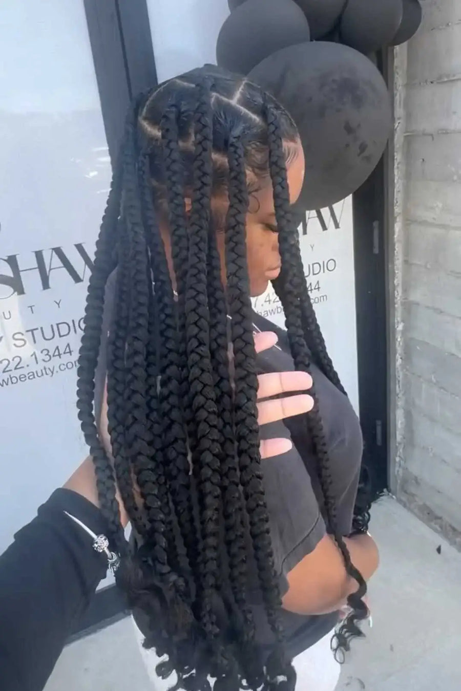 Person with long braided hair in front of a building with visible branding.