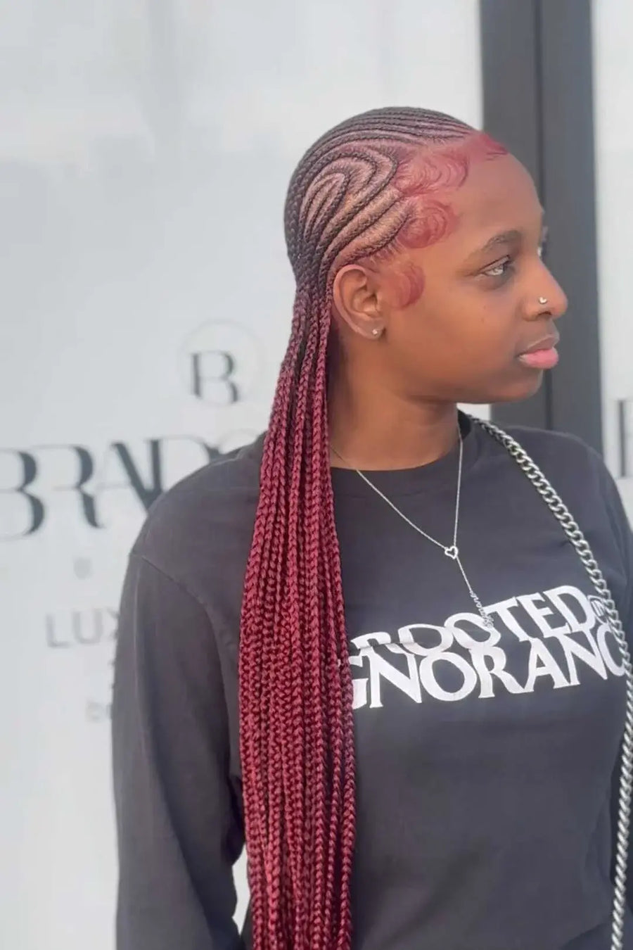 Person with braided hair wearing a black shirt with text, standing in front of a blurred background.