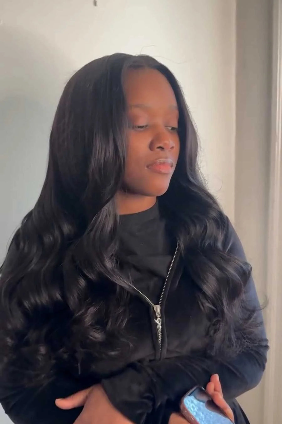 Person wearing a black fur coat holding a phone indoors