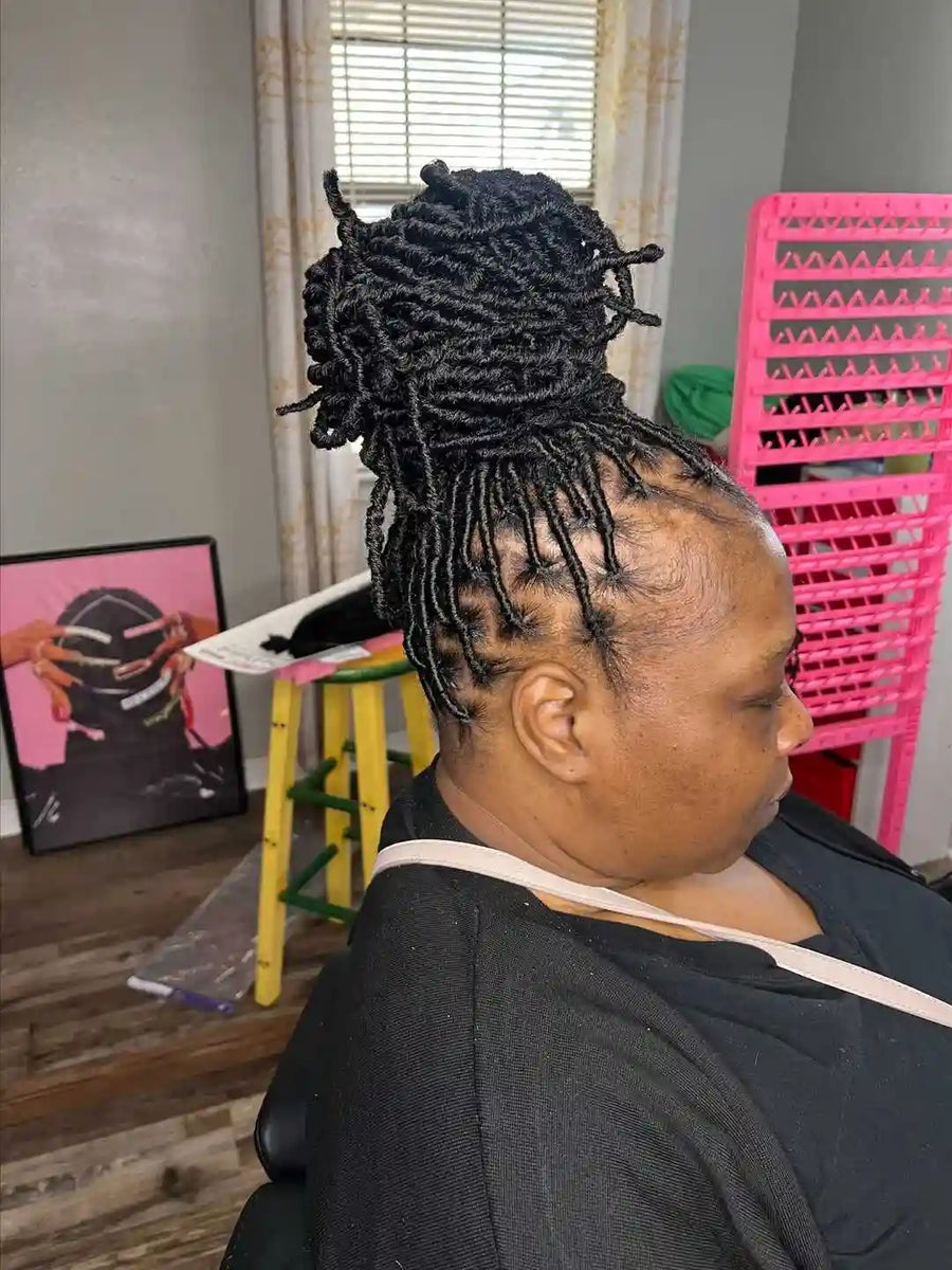Person with styled hair in a salon setting with pink chairs and a mirror.