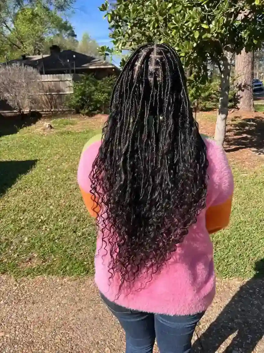Person with long, braided hair wearing a pink sweater outdoors.