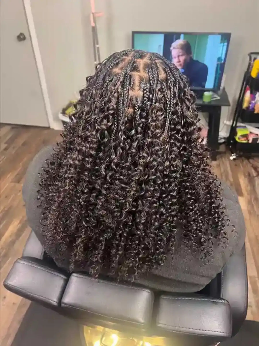 Person with braided hair sitting in a salon chair, with a TV in the background showing a man.