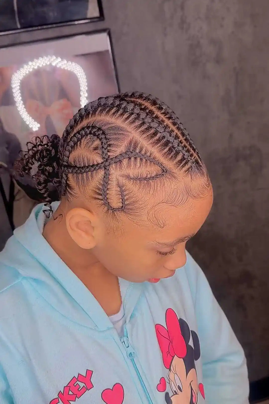 Person with intricate braided hairstyle wearing a light blue hoodie with cartoon character design.