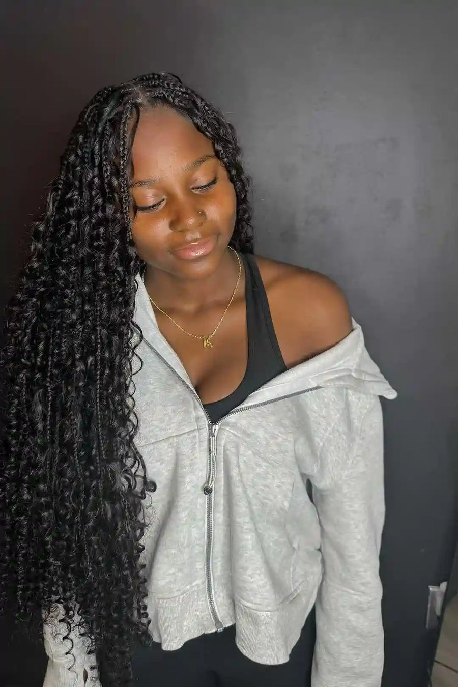 Person wearing a gray hoodie with long braided hair against a dark background
