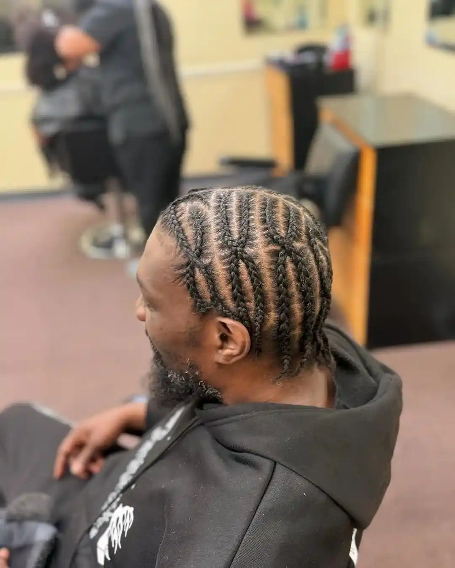 Person with braided hair sitting in a chair, likely in a barbershop setting.