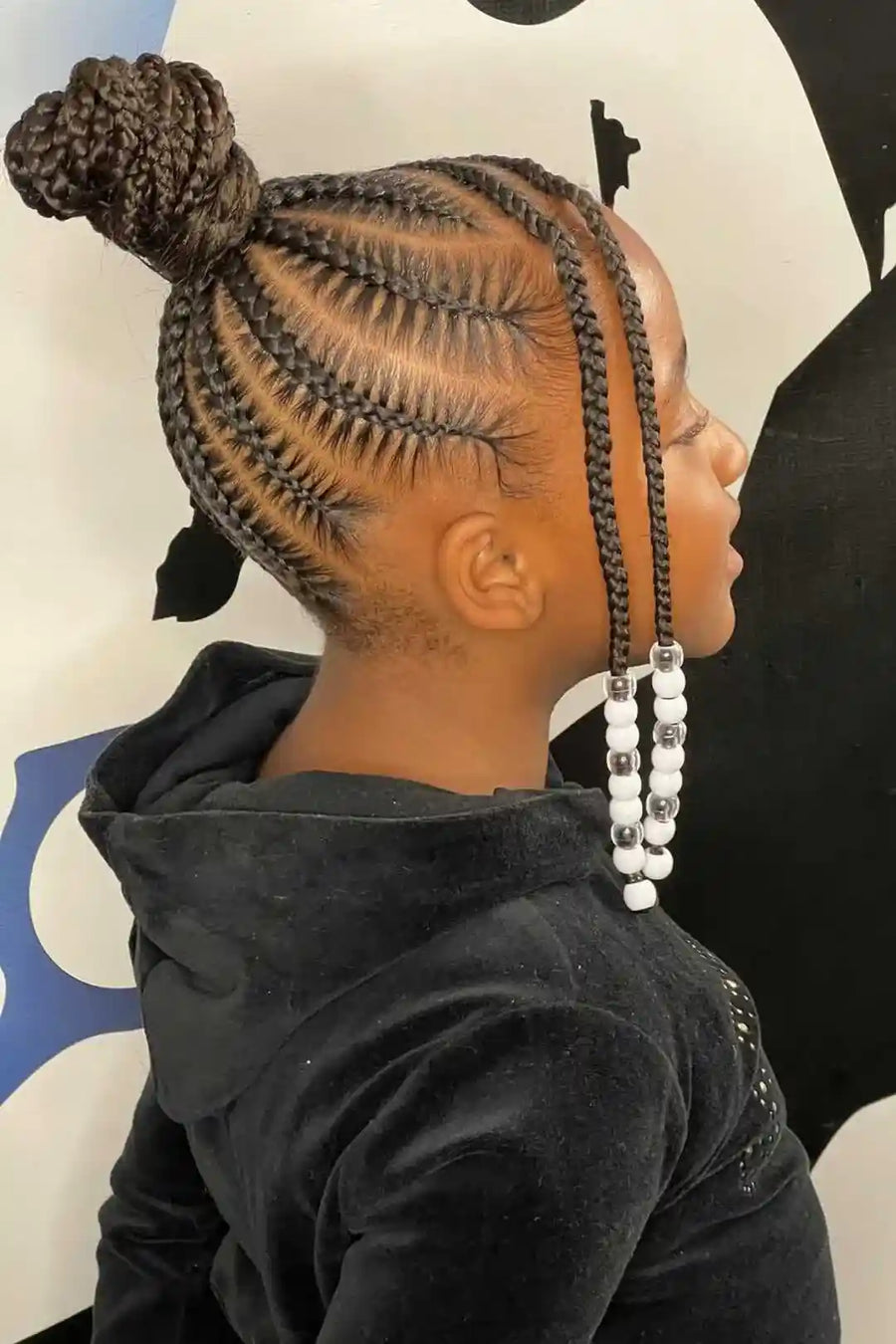 Person with braided hair styled in cornrows with beads, wearing a black hoodie.