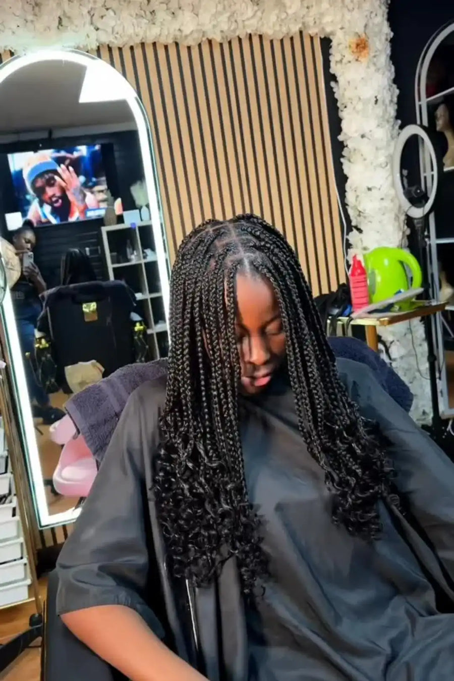 Person with braided hair sitting in a salon chair, watching TV.