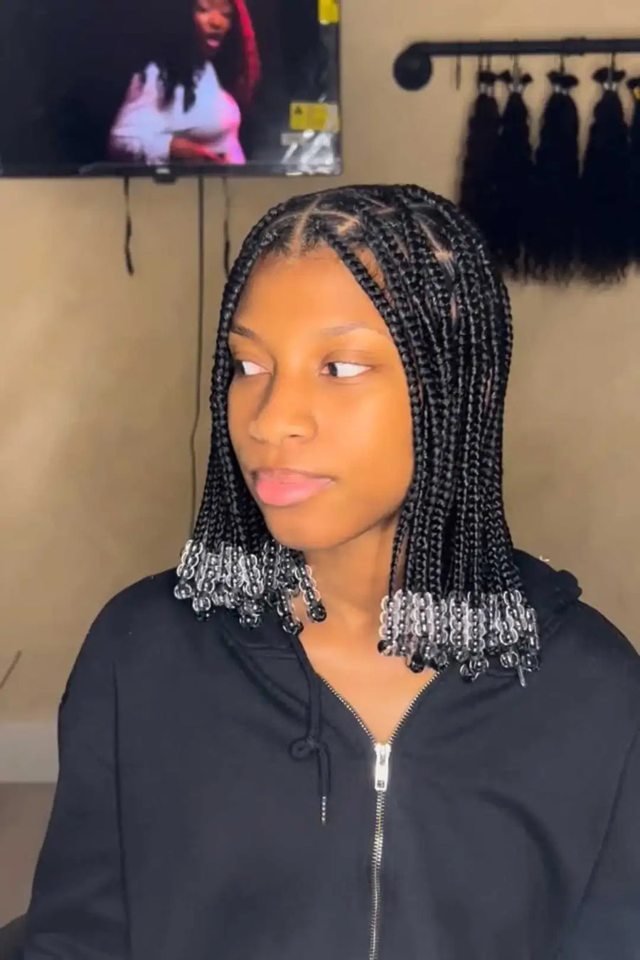 Woman with braided hair in a salon setting with a television screen in the background.