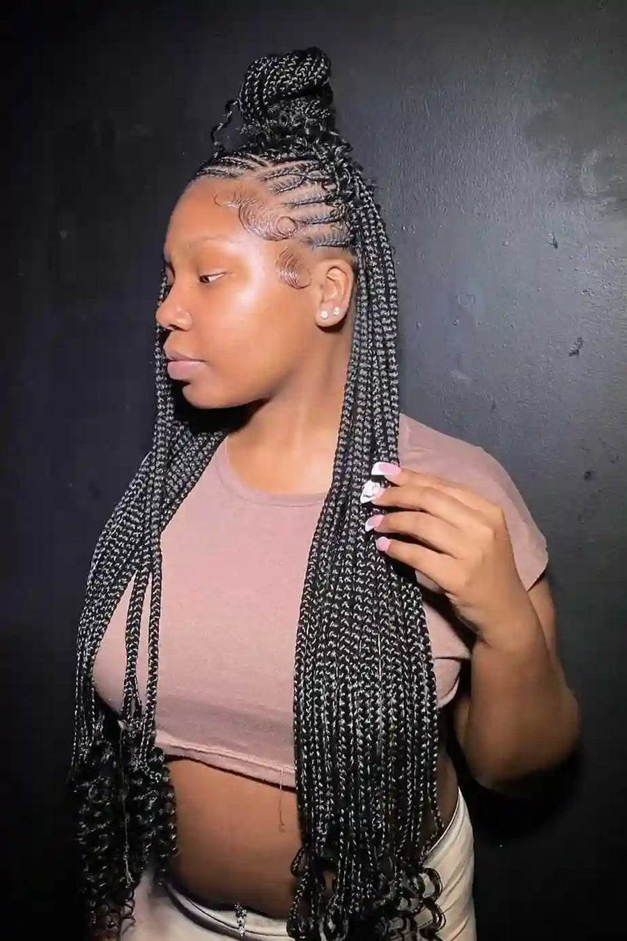 Person with long braided hair wearing a pink top against a dark background