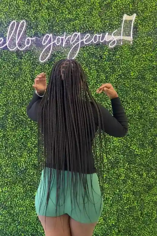 Person with long braided hair standing against a green textured wall with 'hello gorgeous!' text.