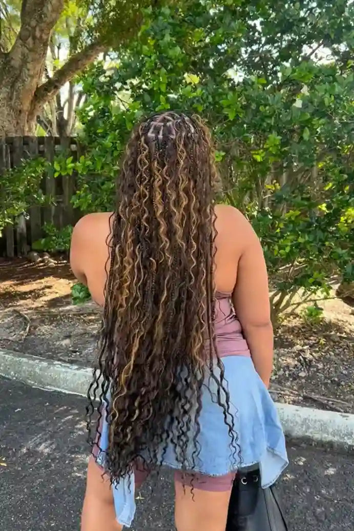 Person with long, styled hair standing outdoors with trees in the background