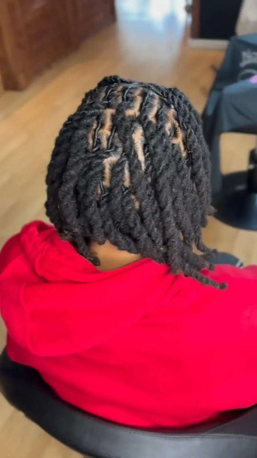 Person wearing a red hoodie with braided hair sitting on a chair.
