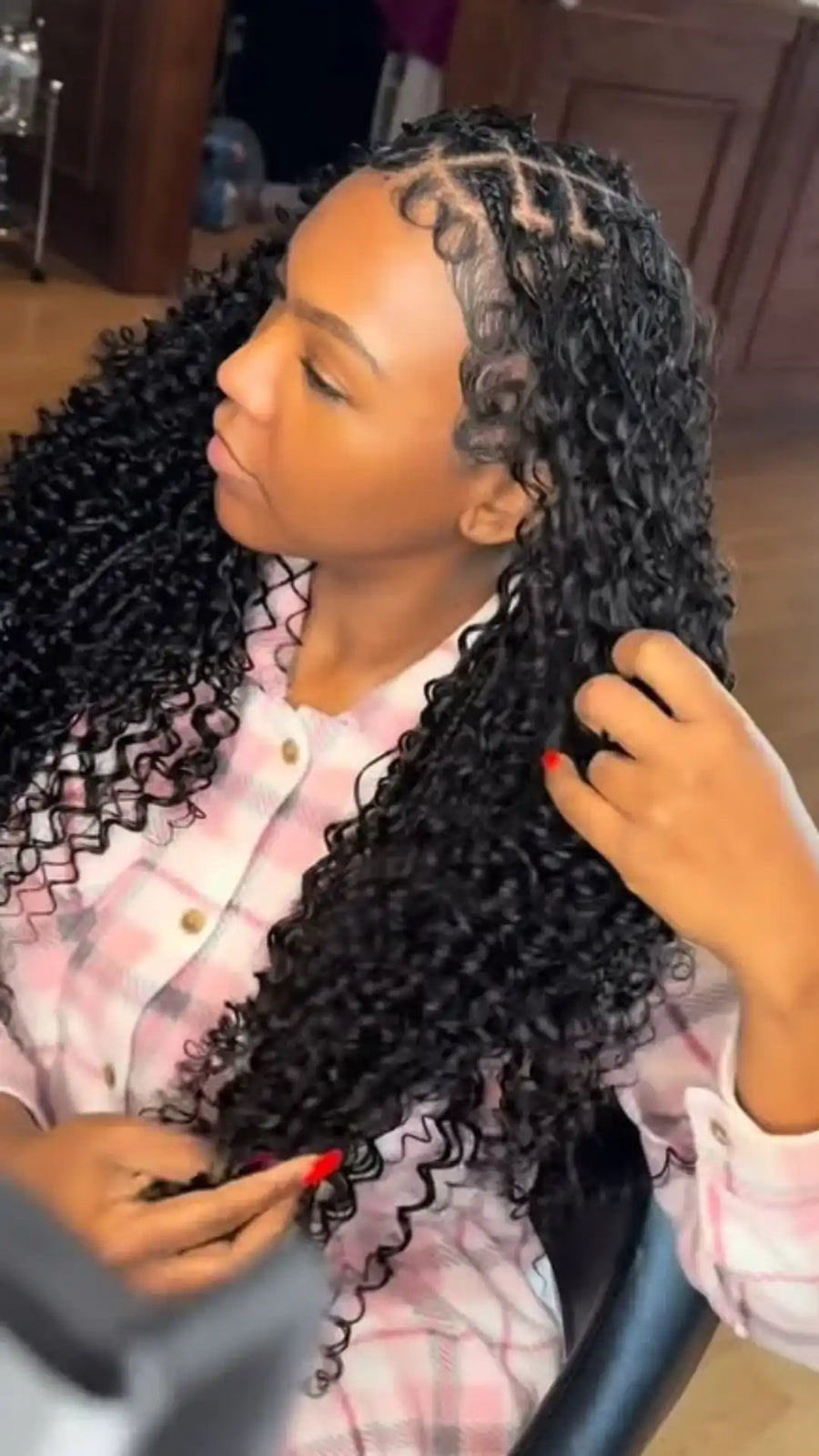 Woman with styled hair sitting in a chair, receiving hair extensions.