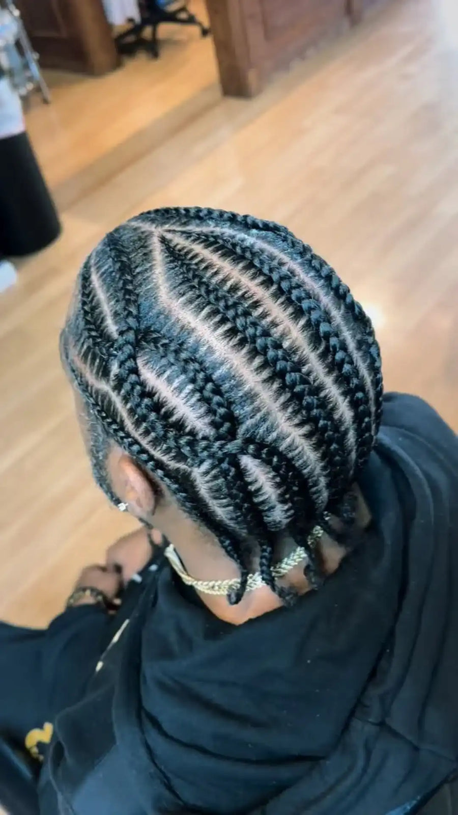 Person with braided hair wearing a black garment indoors.