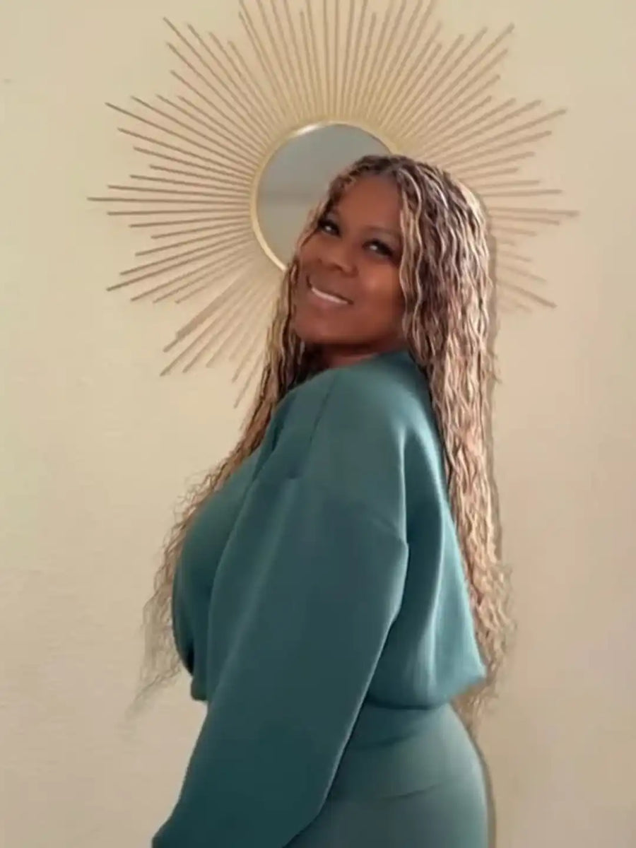 Woman in a teal outfit standing in front of a decorative wall mirror.