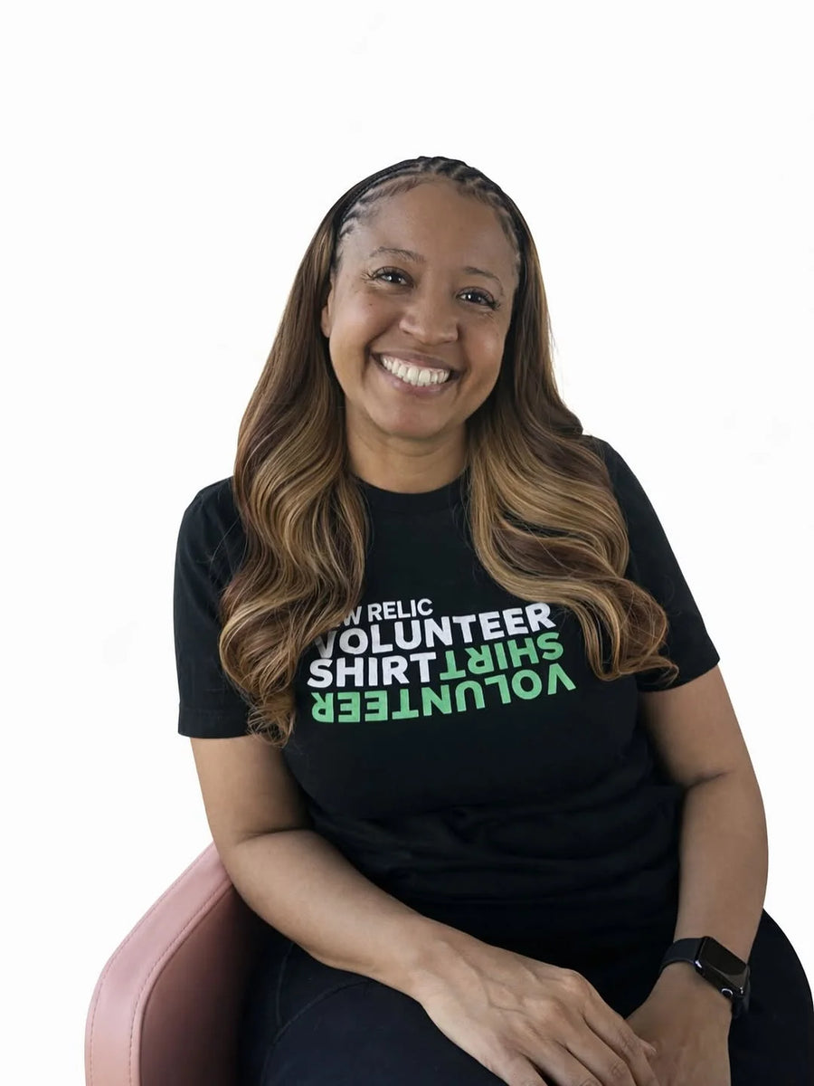 Person wearing a black t-shirt with text, sitting on a pink chair against a white background